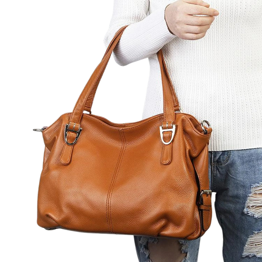 Cognacfarbene Halbmondtasche mit klarer Struktur, getragen zur weißen Strickjacke