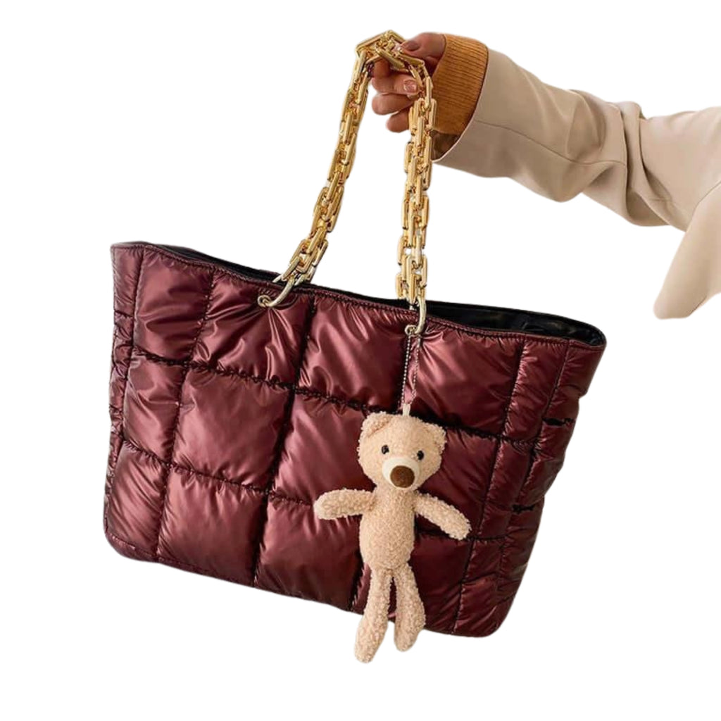 Bordeauxrote gesteppte Handtasche mit Teddy-Anhänger und goldener Kette in der Hand gehalten