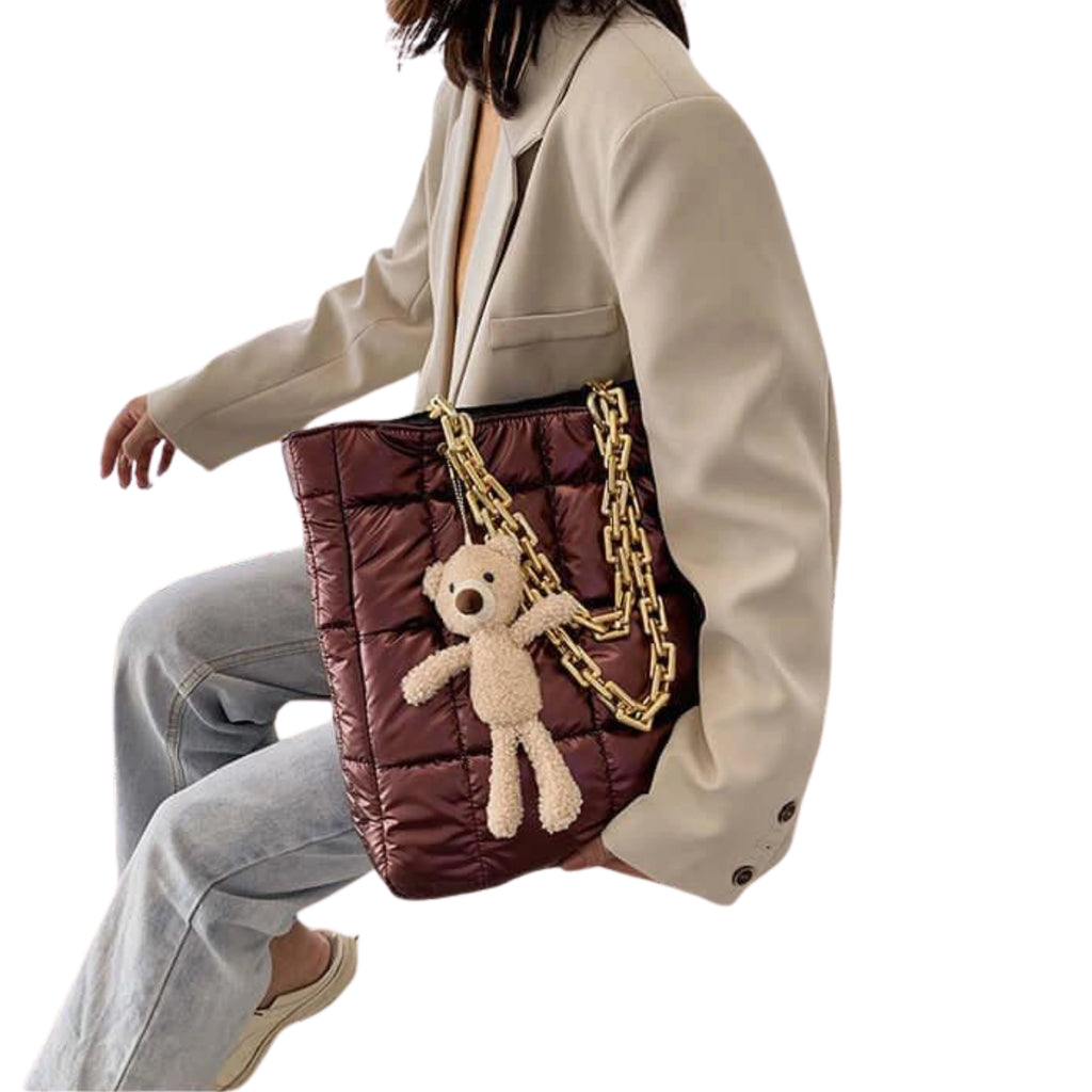 Vertikal getragener Puffy Shopper in Bordeaux mit Plüschteddy, kombiniert mit beiger Jacke und Jeans