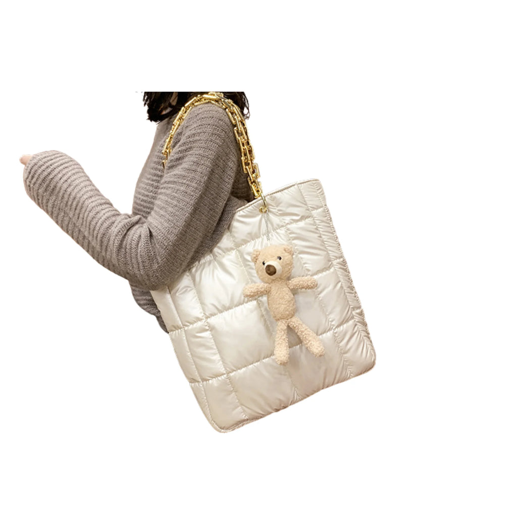 Beigefarbene wattierte Tasche mit goldfarbener Kette und Teddy-Anhänger im Hochformat an Schulter getragen
