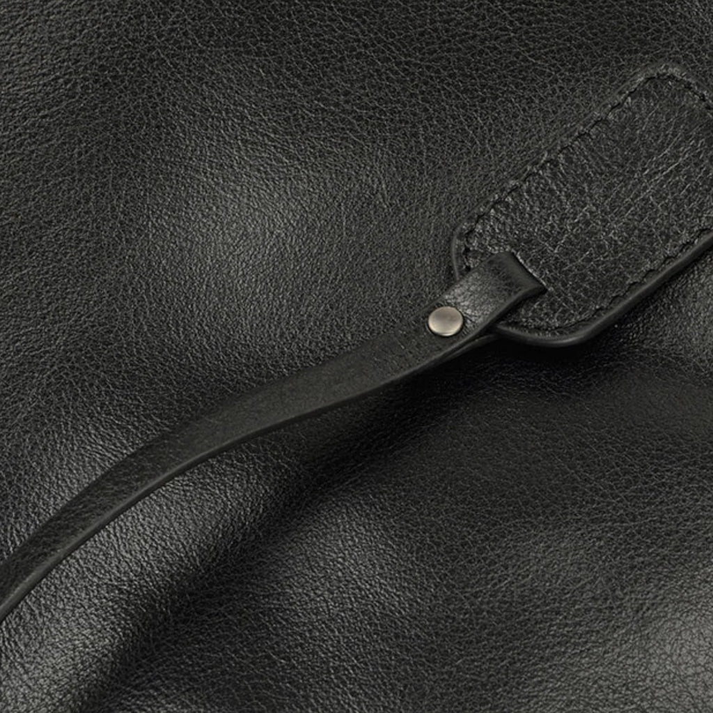 Schwarze Lederoberfläche mit Zugband und Metallniete – feine Verarbeitung sichtbar