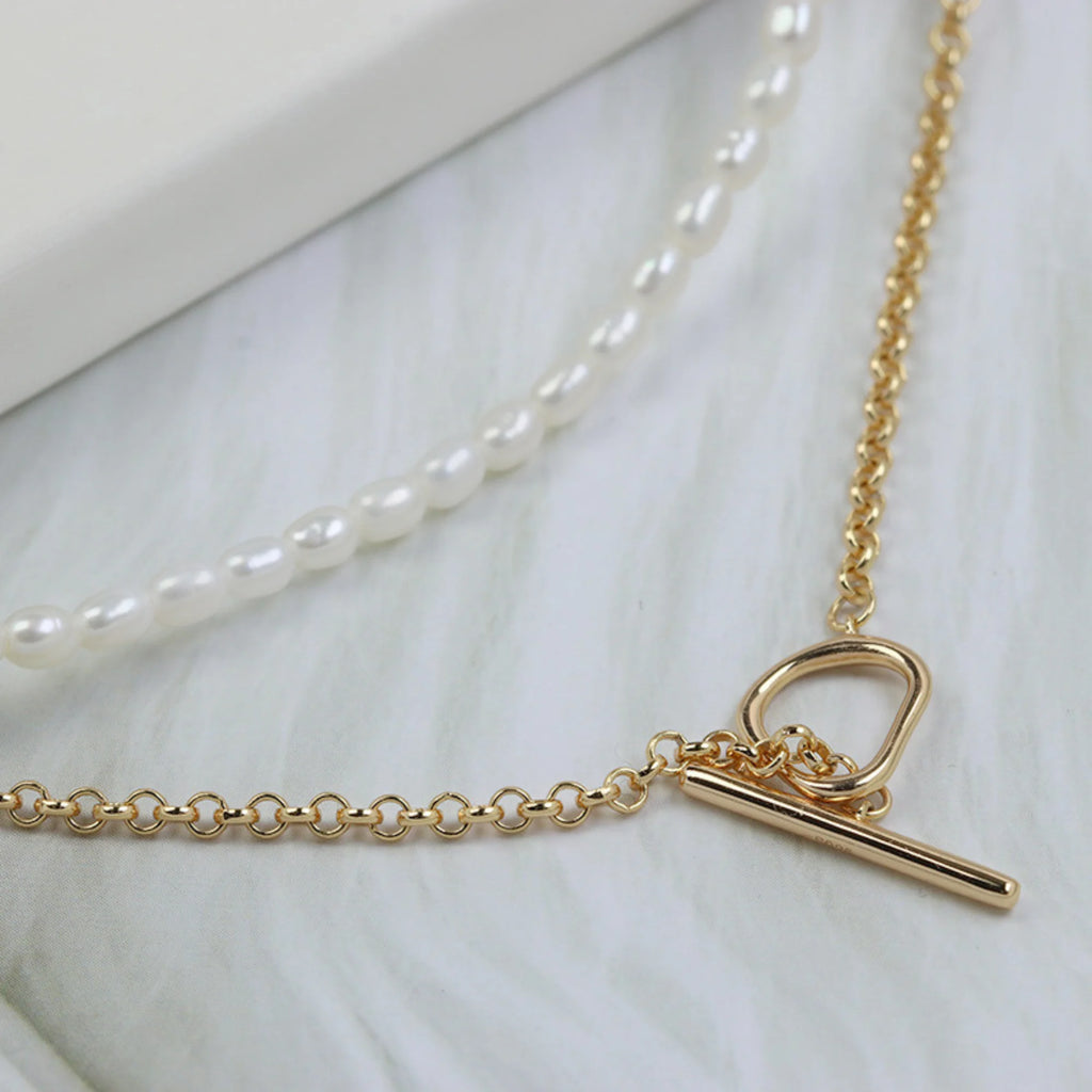 Nahaufnahme des goldenen Knebelverschlusses der Doppelkette mit Perlen und Gliederstruktur auf weissem Grund.