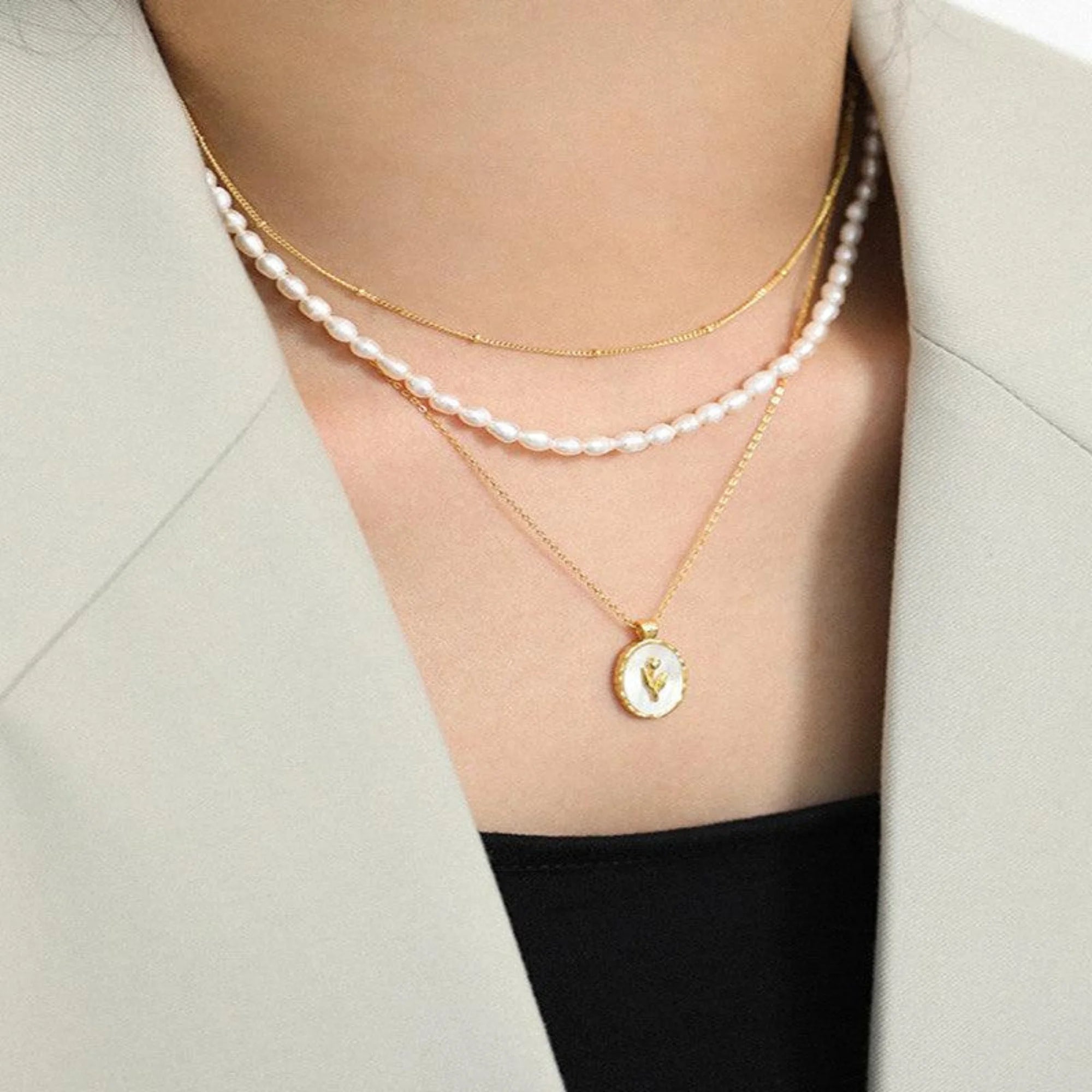 Zweifaches Ketten-Layering mit Perlen- und Goldkette – getragen über einem beigen Blazer