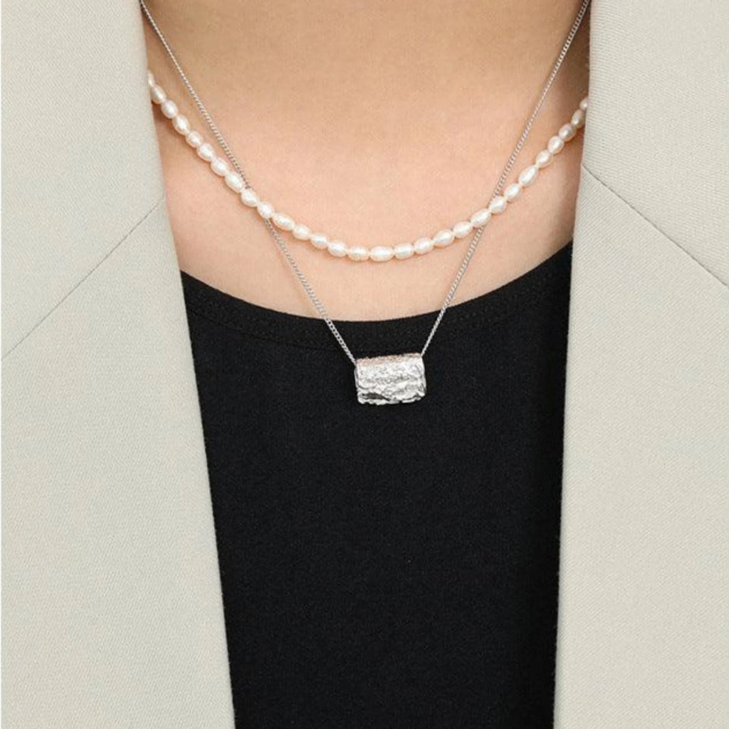 Model mit Layering-Look aus Perlenkette und eckigem Anhänger in Silber – clean und modern gestylt