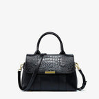 Schwarze Kelly-Tasche mit markanter Kroko-Textur, formstabiler Silhouette und kurzem Griff