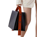 Moderne Lederhandtasche mit breitem orangefarbenem Riemen und Ösen, getragen an der Hand