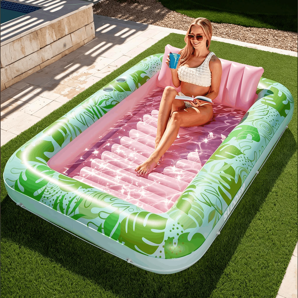 Aufblasbares Tanning Pool Bett Variante Pink-Grün mit glitzernder Wasserfläche – Frau sitzt mit Getränk und Buch, ergonomisches Nackenkissen und zwei Getränkehalter integriert, Lieferung in die Schweiz