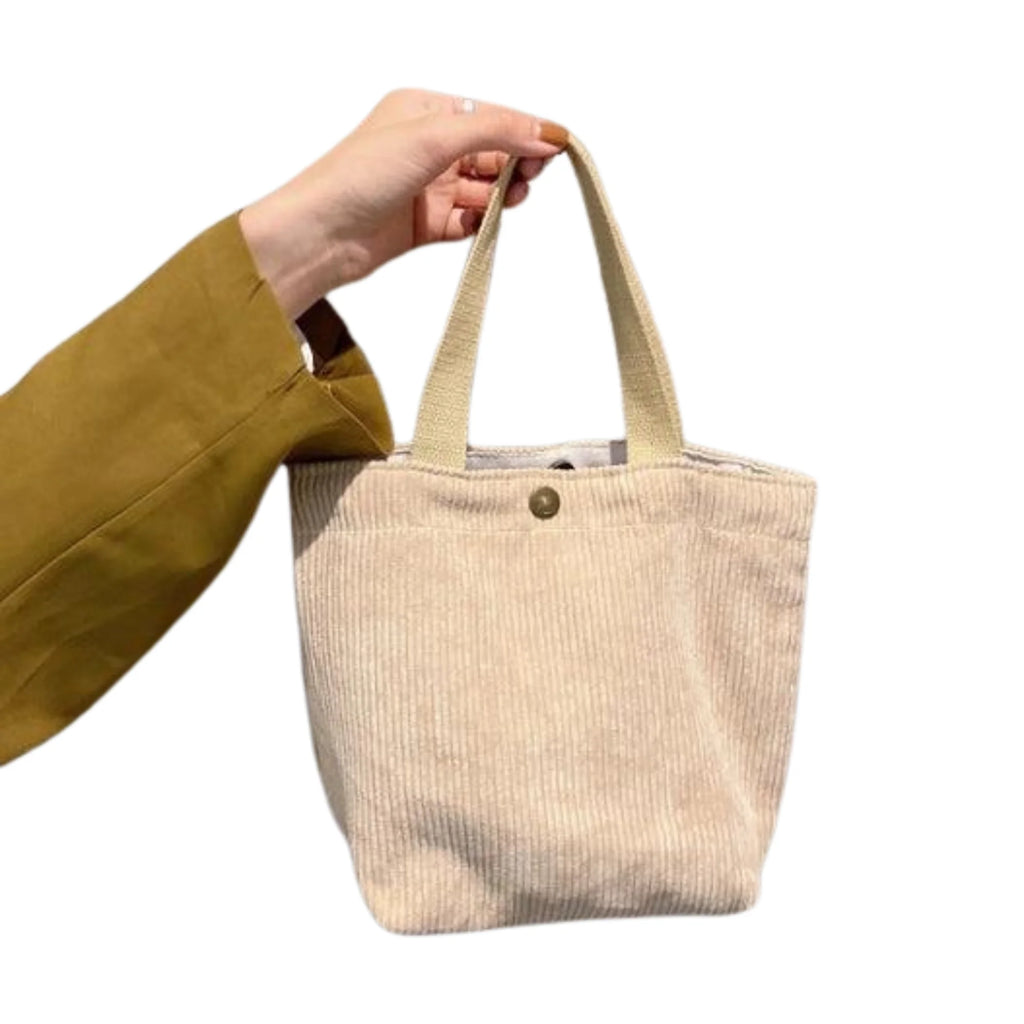 Beige Cordtasche mit goldenem Druckknopf, dezent in der Hand gehalten