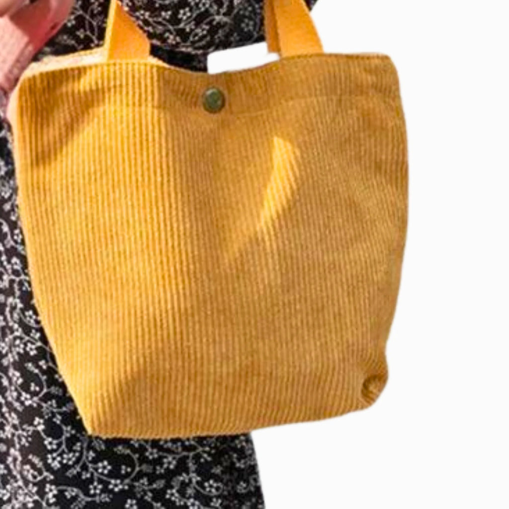 Cordtasche in hellem Gelb mit weichem Griff, über geblümtem Kleid getragen