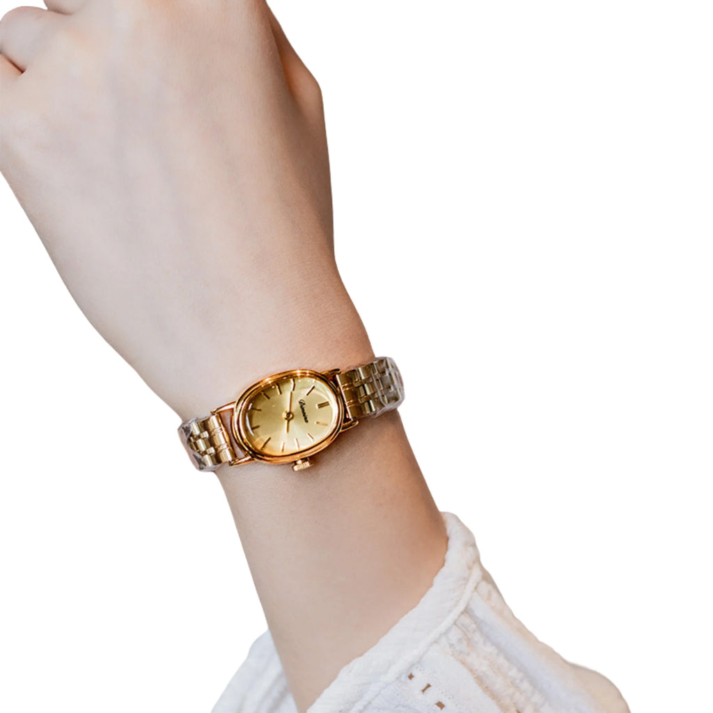 Ovale Uhr mit goldfarbenem Zifferblatt und zweifarbigem Gliederarmband am Handgelenk.