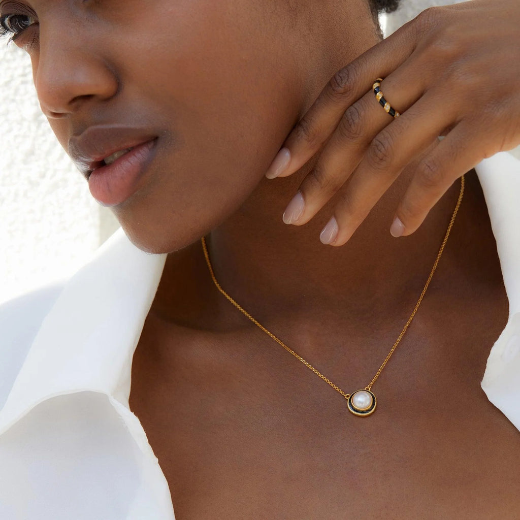 Nahaufnahme einer minimalistischen Kette mit runder Perle und mattschwarzer Fassung in Gold auf der Haut getragen