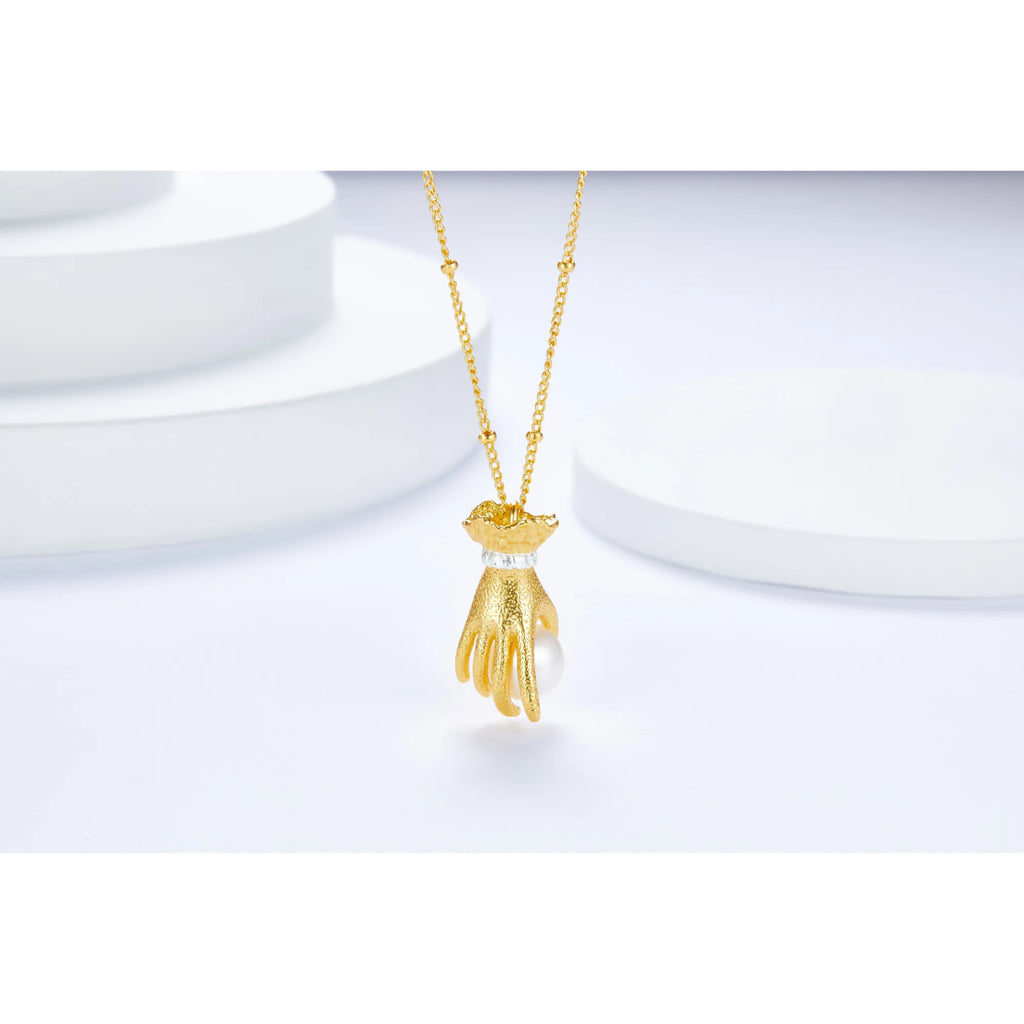 Studiobild einer goldenen Kette mit detailliertem Handanhänger, der eine echte Perle umfasst – ruhige, klare Darstellung