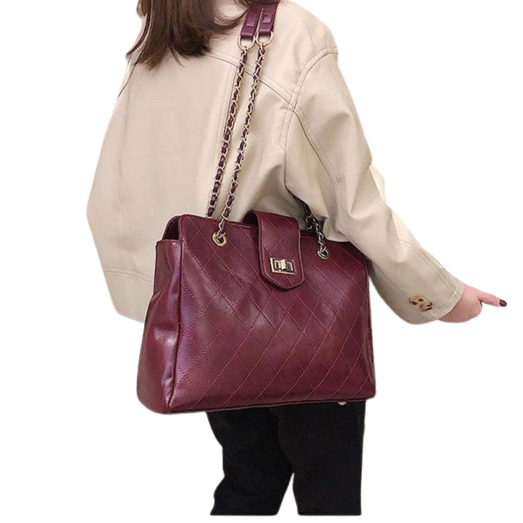 Tiefrote Schultertasche mit Kette – glänzende Oberfläche und starker Kontrast zum Mantel