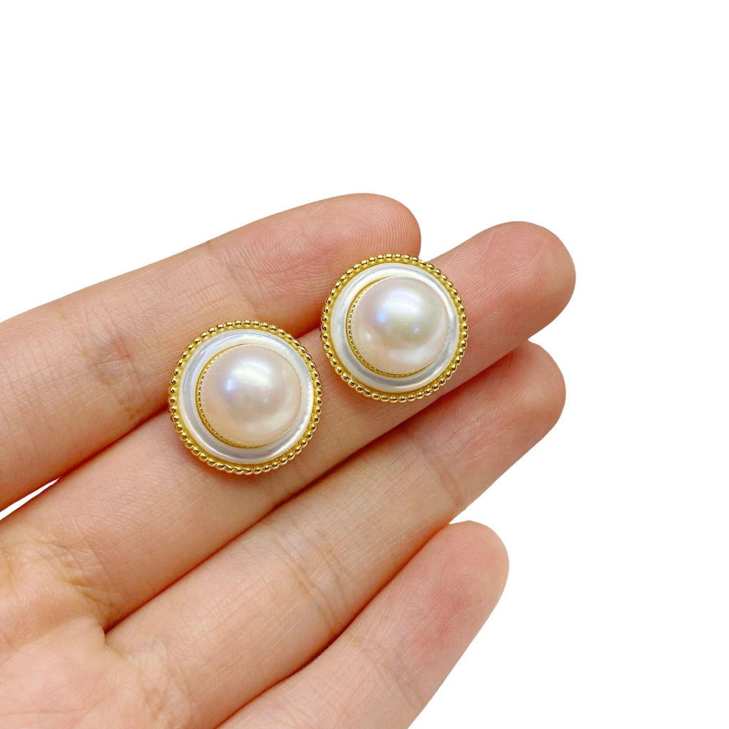 Goldene Ohrstecker mit klarer Kreisstruktur und echter Perle – getragen am Finger