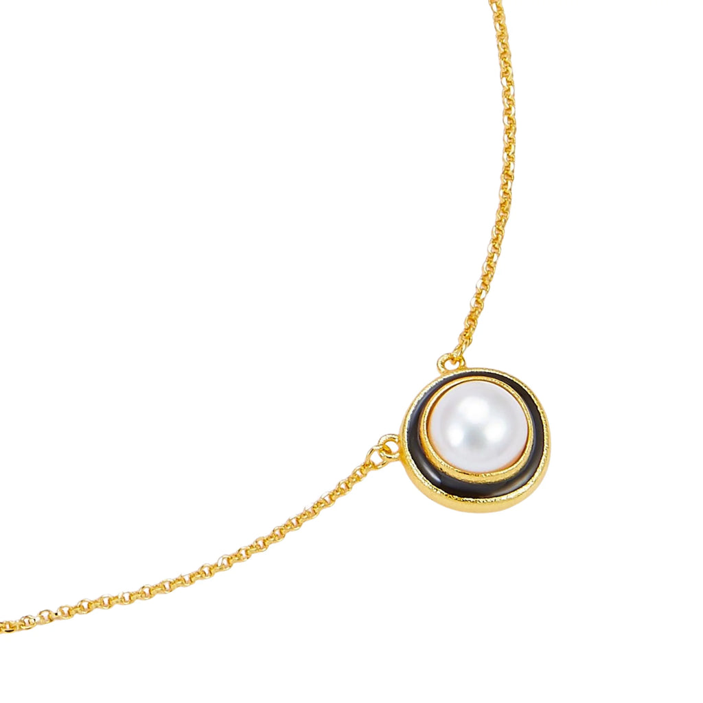 Detailansicht des goldenen Anhängers mit zentraler weisser Perle und umlaufendem mattschwarzen Kreis auf feiner Gliederkette