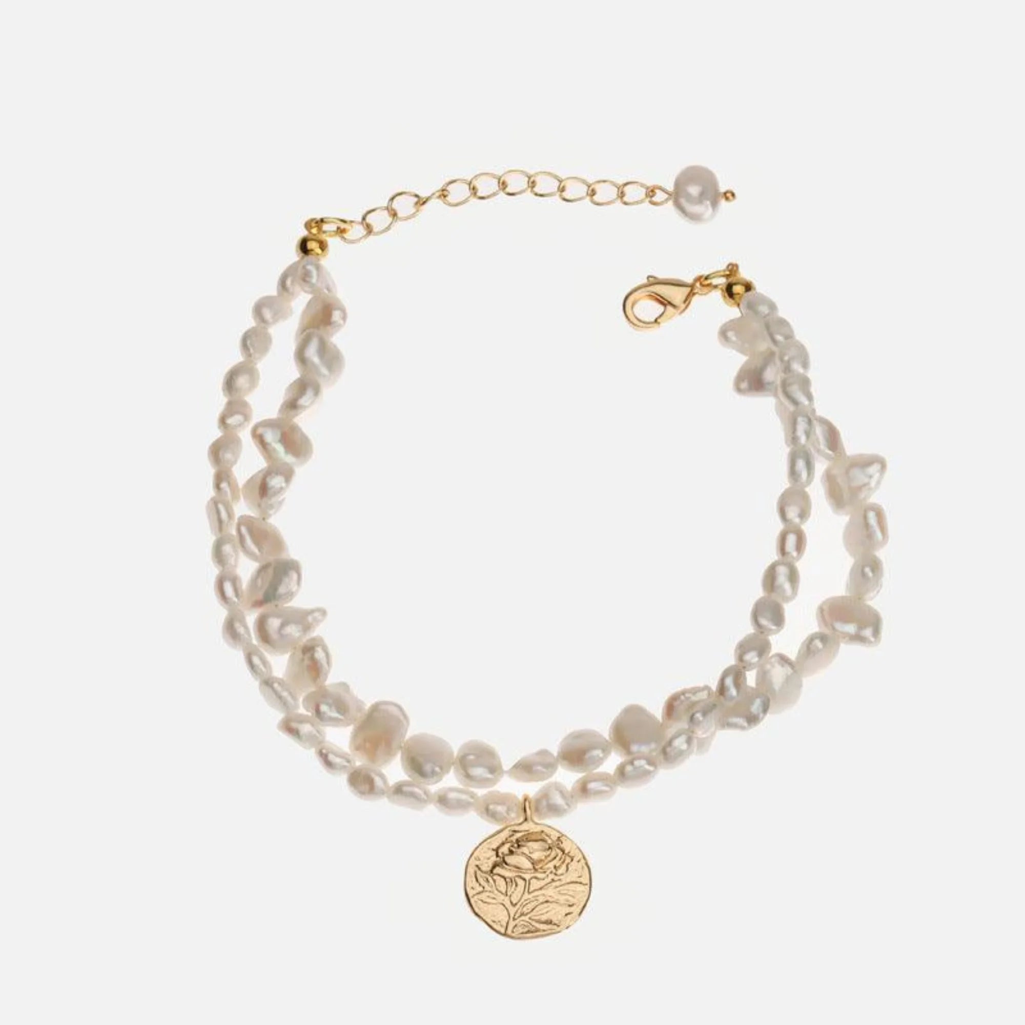 Perlenarmband mit goldenem Anhänger am Handgelenk getragen – klar, ruhig, unregelmässig