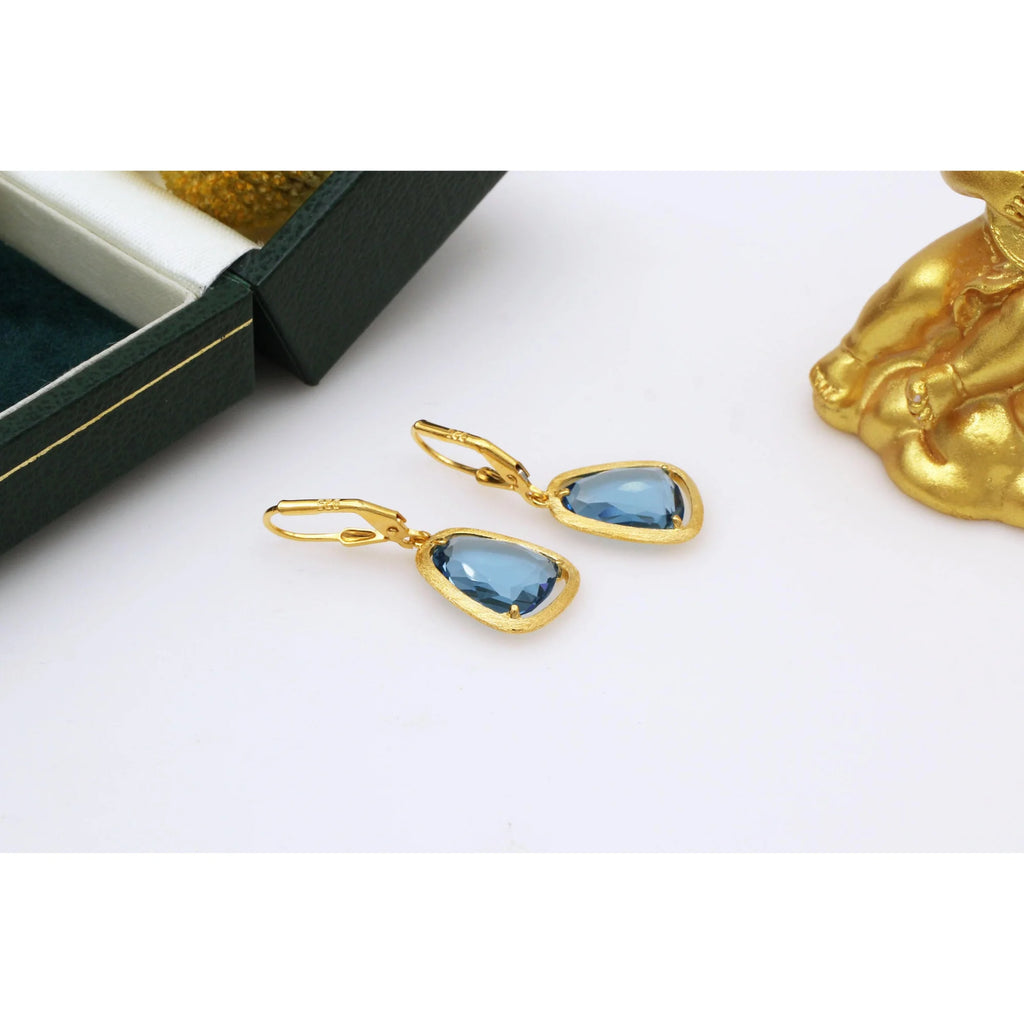 Ohrhängerpaar in goldener Fassung mit blauer Fläche, flach neben Etui positioniert