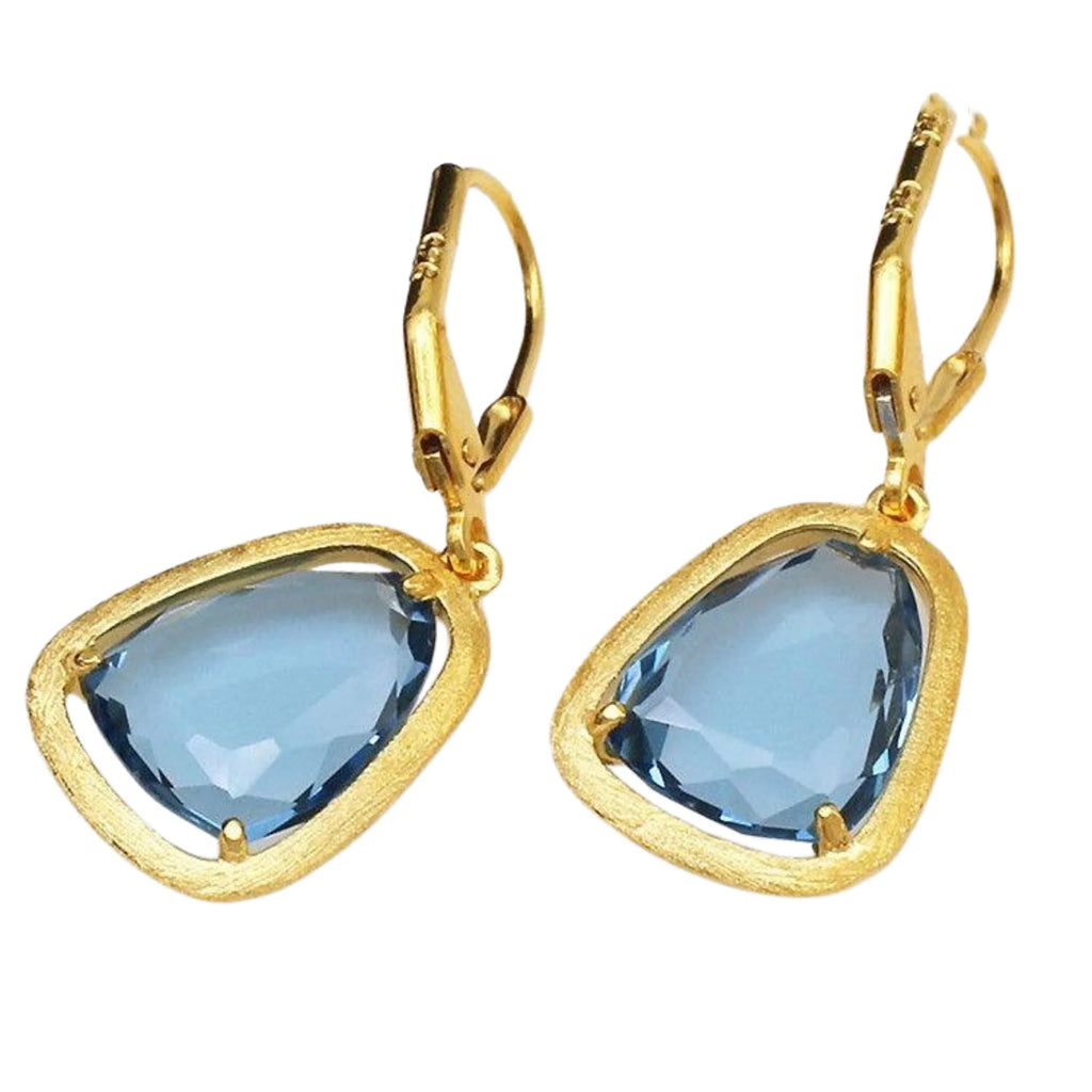 Nahaufnahme zweier goldfarbener Hänger mit asymmetrischem blauem Glas