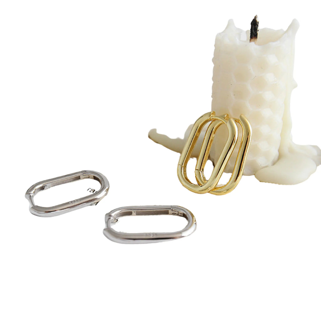 Ovale Ohrringe in Gold und Silber vor Wabenkerze arrangiert – neutral inszeniert.