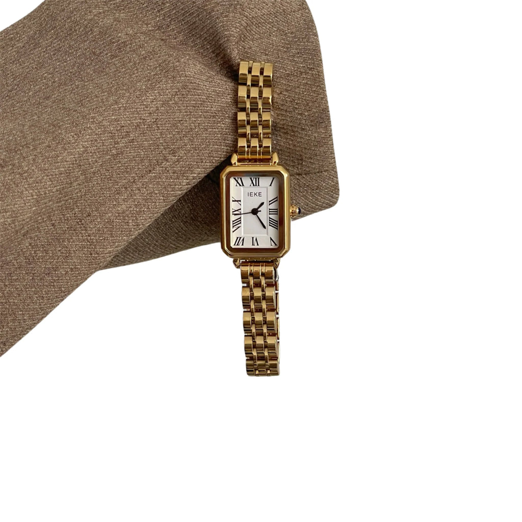 Goldene Uhr mit Gliederband von oben fotografiert, getragen über braunem Ärmel.