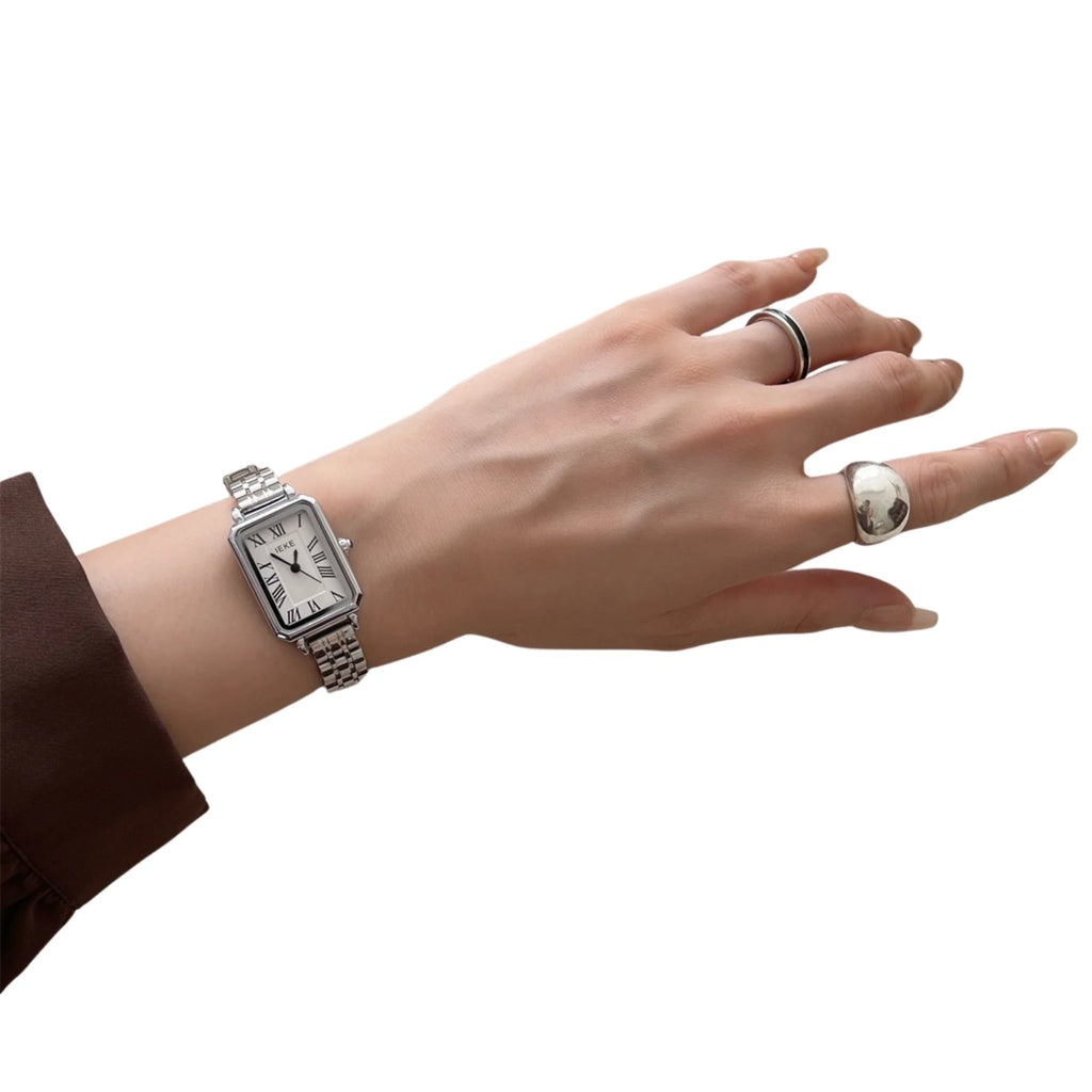 Silberne rechteckige Uhr am Handgelenk mit silbernem und schwarzem Ring.