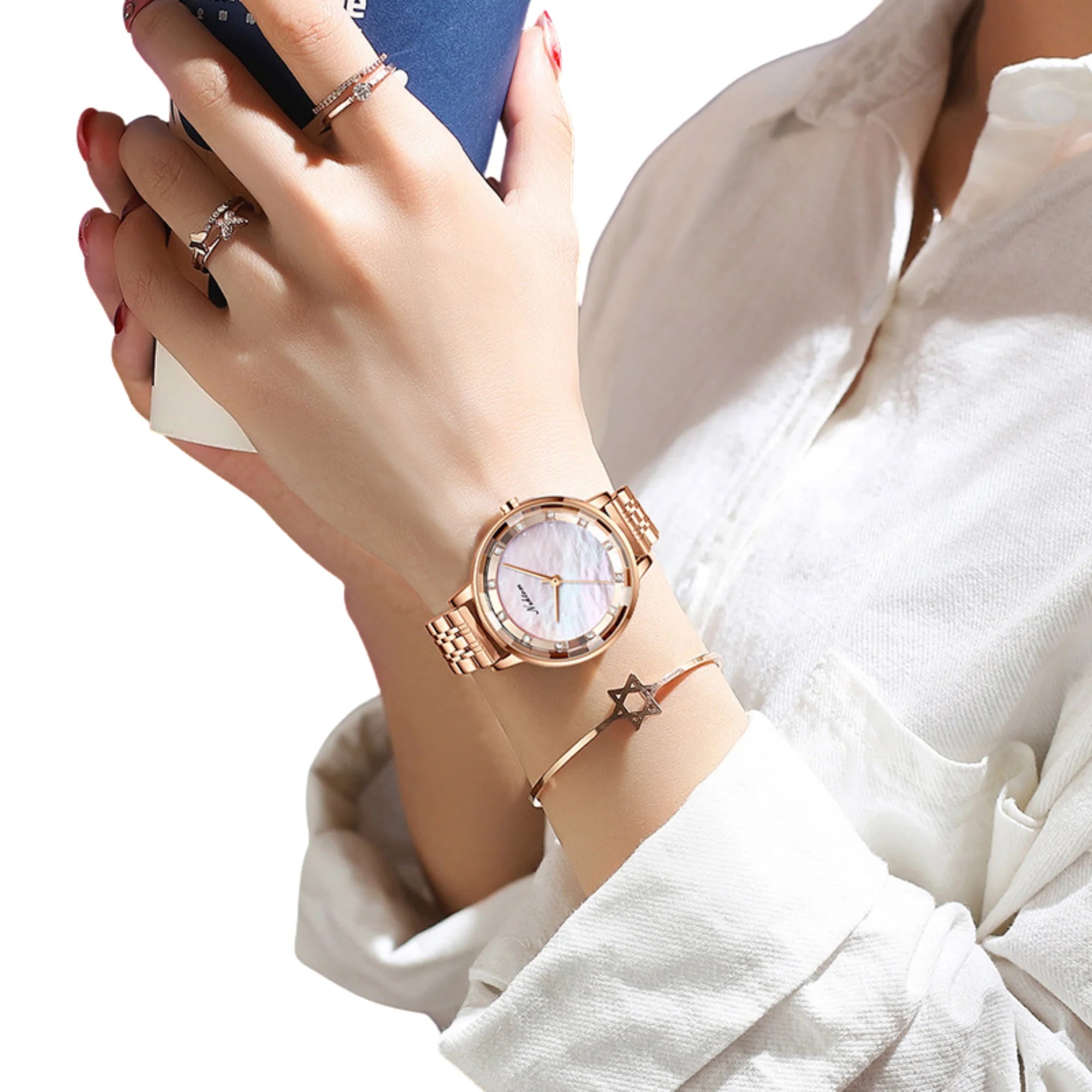 Uhr in Roségold mit perlmuttartigem Zifferblatt, getragen mit Armreif und Ringen.