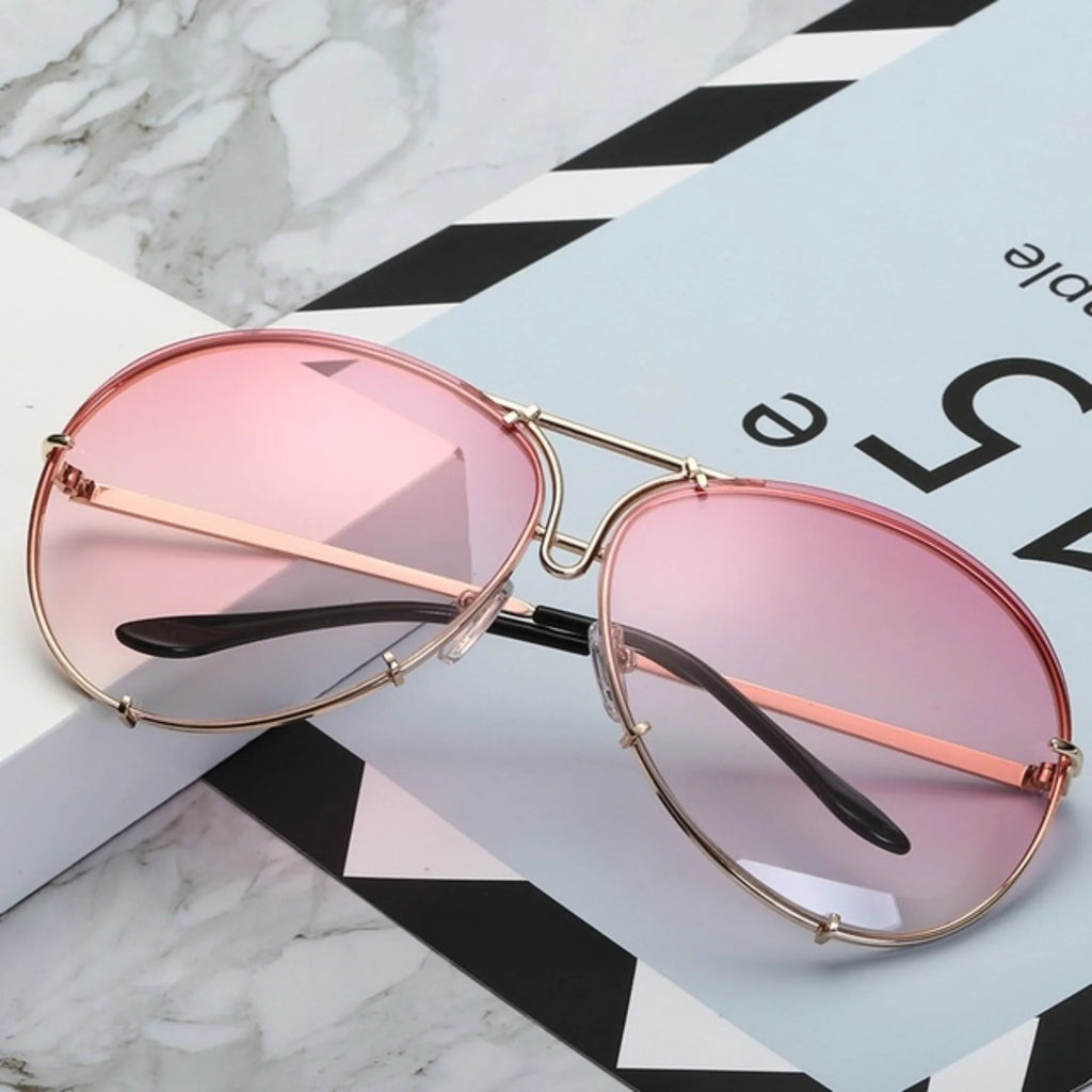 Sonnenbrille mit rosa Verlaufsglas und feinem Goldrahmen auf Marmorfläche