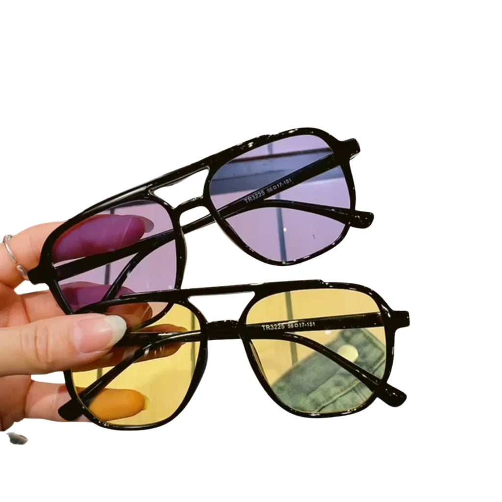 Zwei Sonnenbrillen in Schwarz mit lila und gelben Gläsern – gehalten in der Hand.